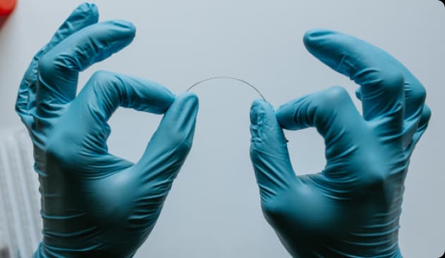 Mãos com luvas segurando uma agulha fina, como se fosse dobrando. A agulha é utilizada para o tratamento de agulhamento seco.